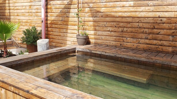 A wooden deck with a hot spring pool, surrounded by potted plants and a wooden wall. - Duplex Avec Jardin, Piscine, Terrasse, 3 Chambres (Palavas-les-Flots)