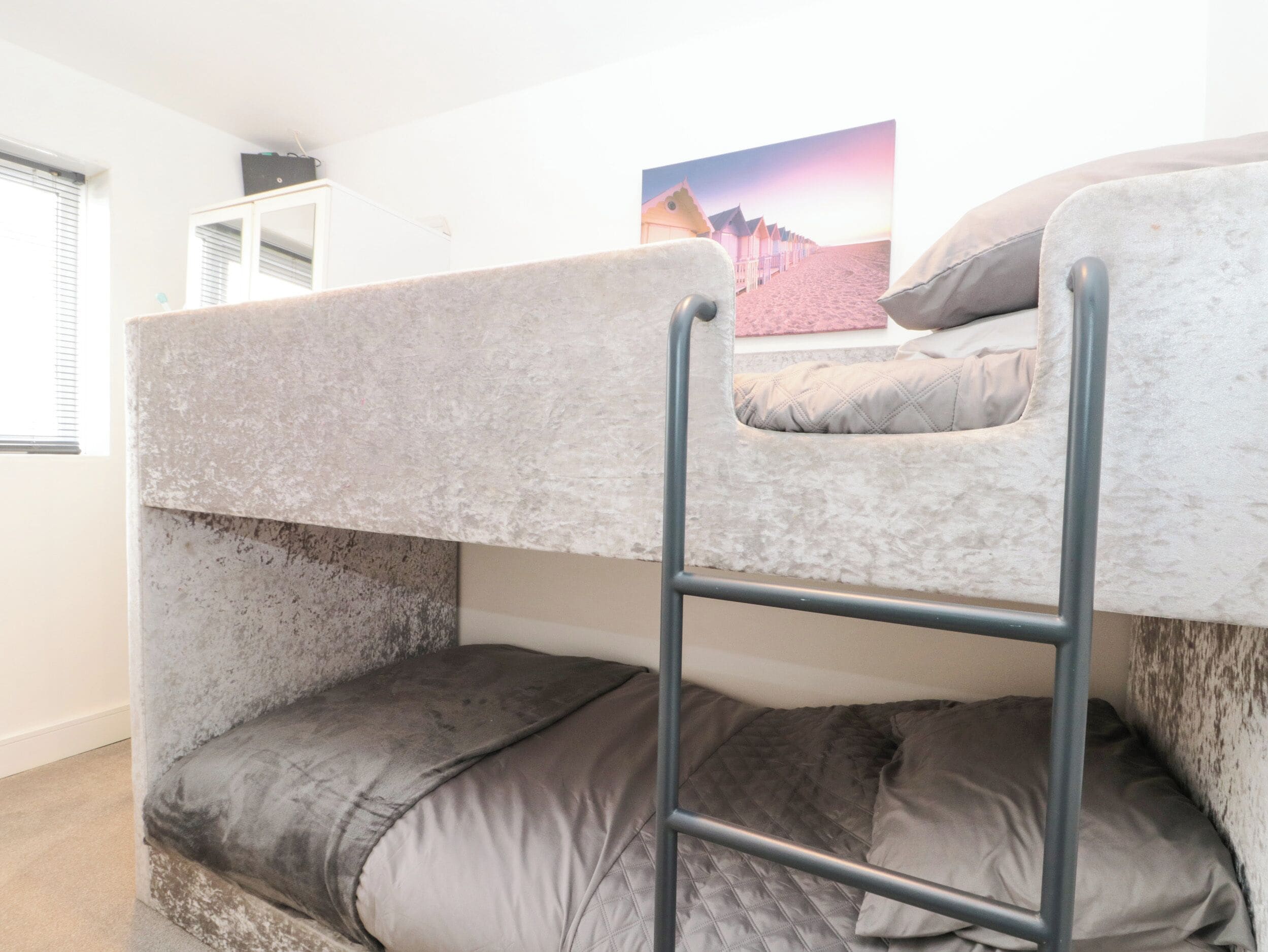 A bunk bed with a ladder, a window with blinds, and a picture on the wall.