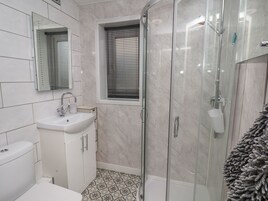 A modern bathroom with a glass shower enclosure, a sink with a mirror, and patterned floor tiles.