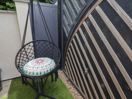 Un sillón hamaca con un cojín estampado, una reja de metal negro y una pequeña sección de césped artificial.