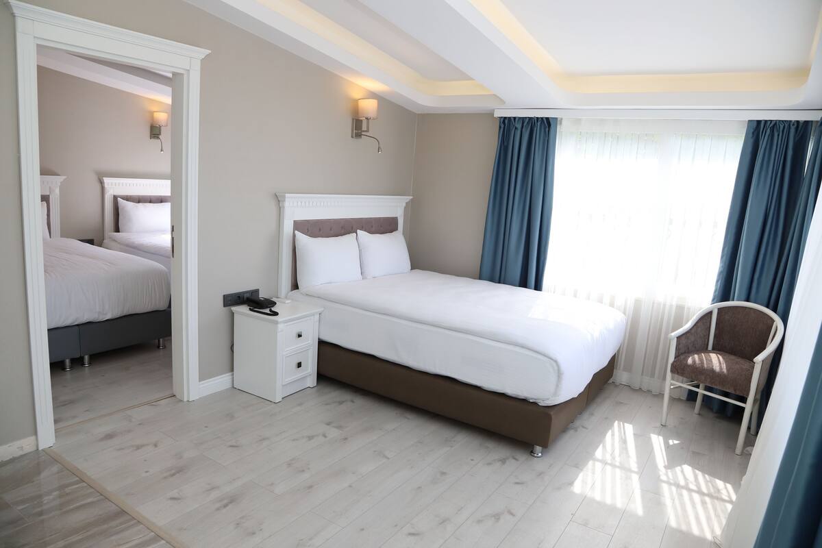 A modern bedroom with a large bed, a bedside table, a chair, and a window with curtains.