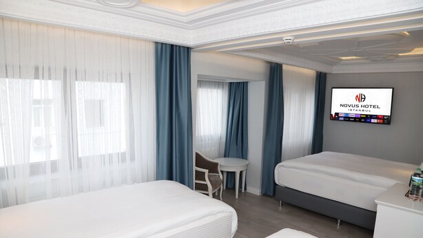 A hotel room with two beds, a desk, a chair, a TV, and a minibar. - Novus Hotel (Istanbul)