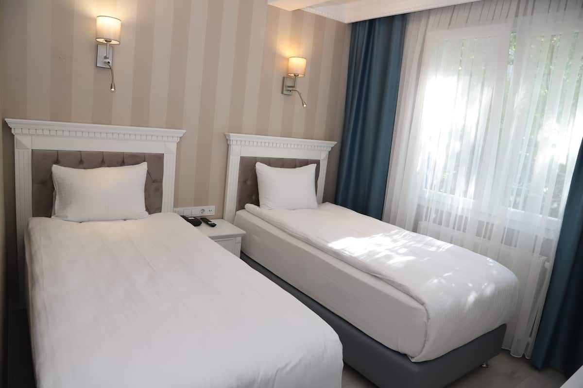 A hotel room with two beds, a nightstand, a wall-mounted lamp, and a window with curtains.