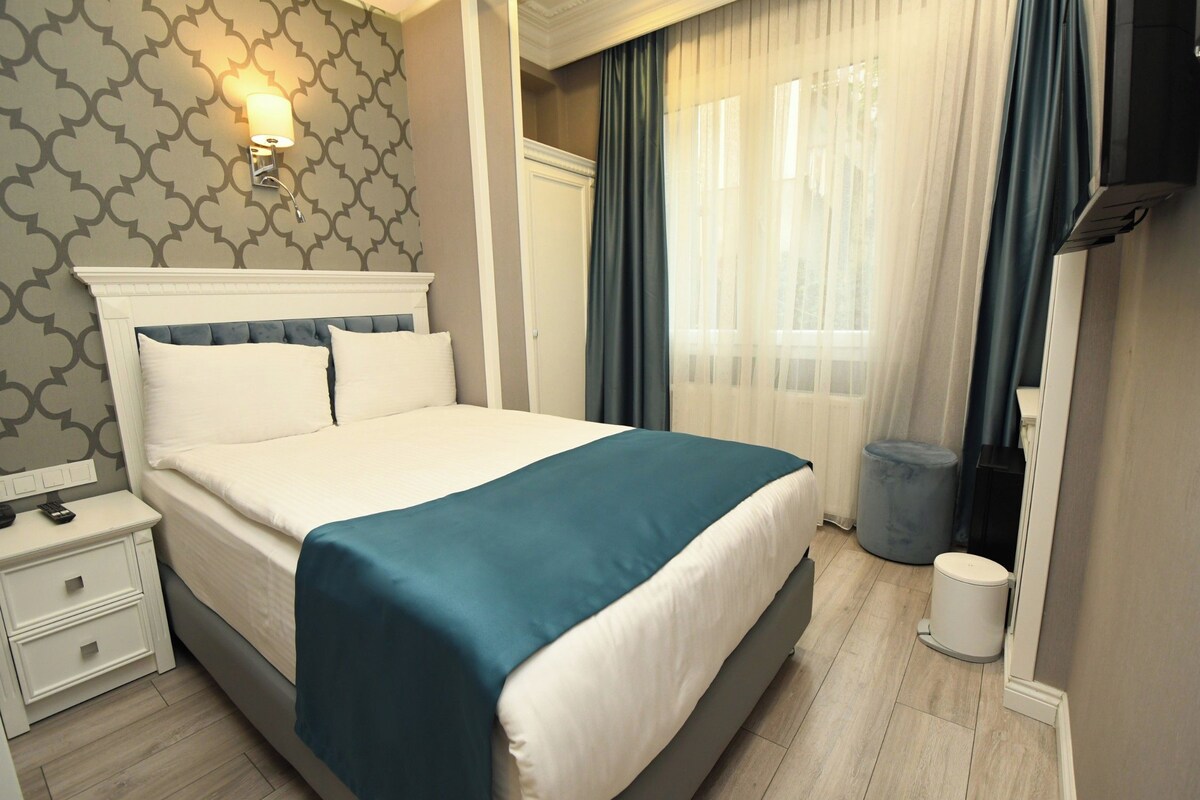 Una habitación de hotel con cama, mesita de noche y lámpara de pared.
