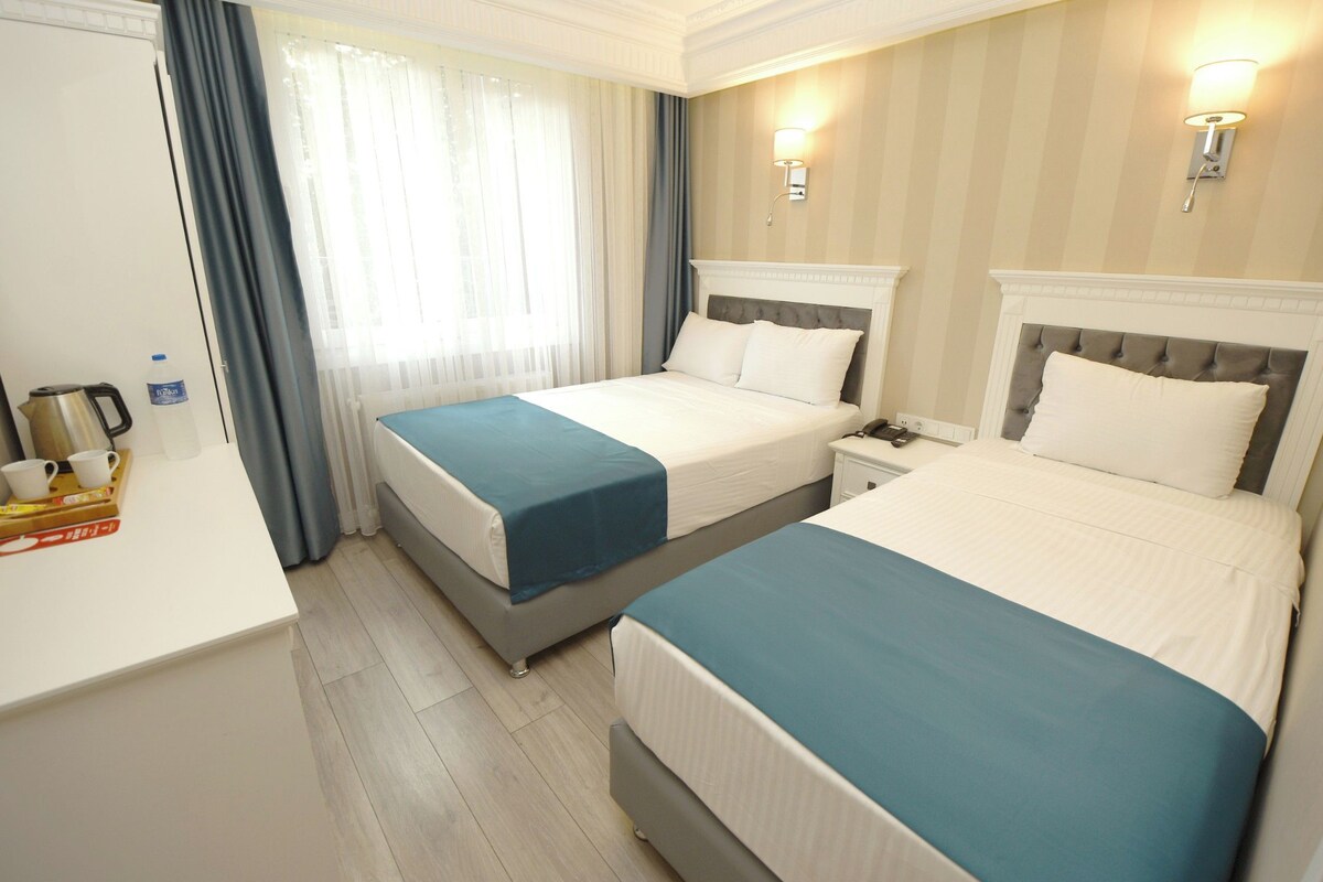 Habitación de hotel con dos camas, un escritorio, una tetera y una botella de agua.