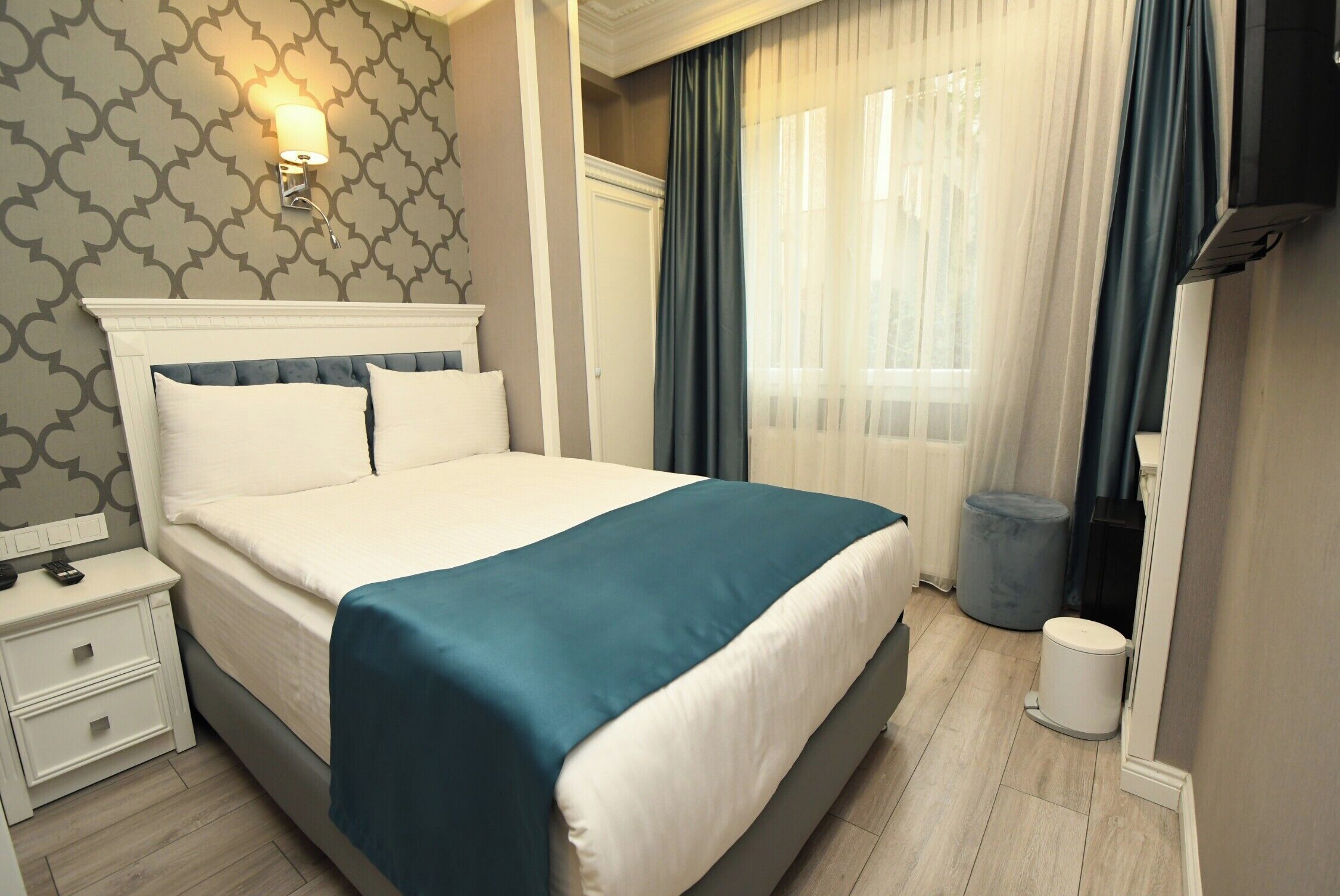 A hotel room with a bed, bedside table, and a wall-mounted light fixture.