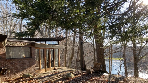 Una baita con ingresso tramite porta in vetro, un sentiero in pietra che conduce a un molo e vista su un lago circondato da alberi.