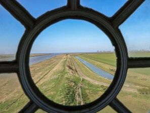 Uitzicht door een rond raam op een landelijk landschap met velden, een rivier en een verre horizon.