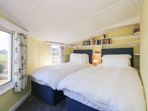 Een slaapkamer met twee bedden, een raam met gordijnen, een boekenplank en een lamp.