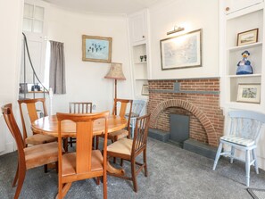 Een eetruimte met een ronde houten tafel en stoelen, een meten haard en wandplanken met ingelijste foto's.