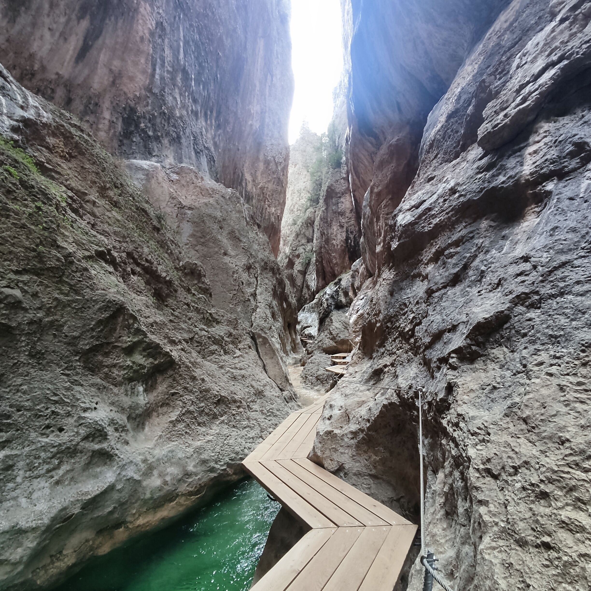 Un cañón estrecho con una pasarela de madera y una pequeña poza de agua.