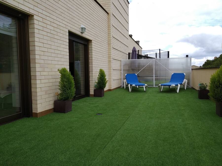 En terrasse med græs, to blå liggestole og krukker med planter.