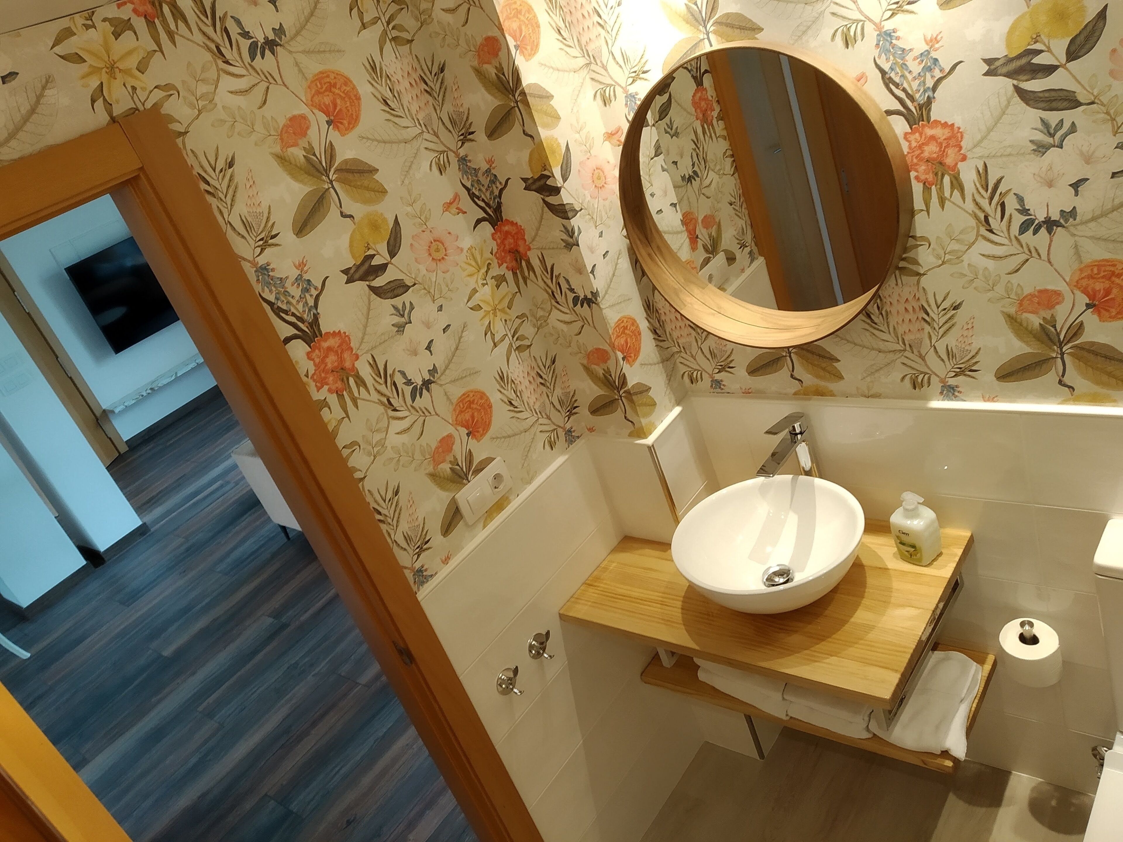 Une salle de bain avec un meuble-lavabo en bois, un lavabo blanc, un miroir et un papier peint à motifs floraux.