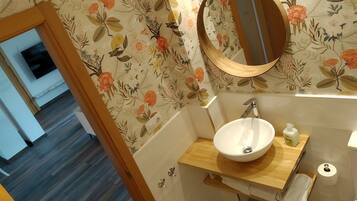 Une salle de bain avec un meuble-lavabo en bois, un lavabo blanc, un miroir et un papier peint à motifs floraux.