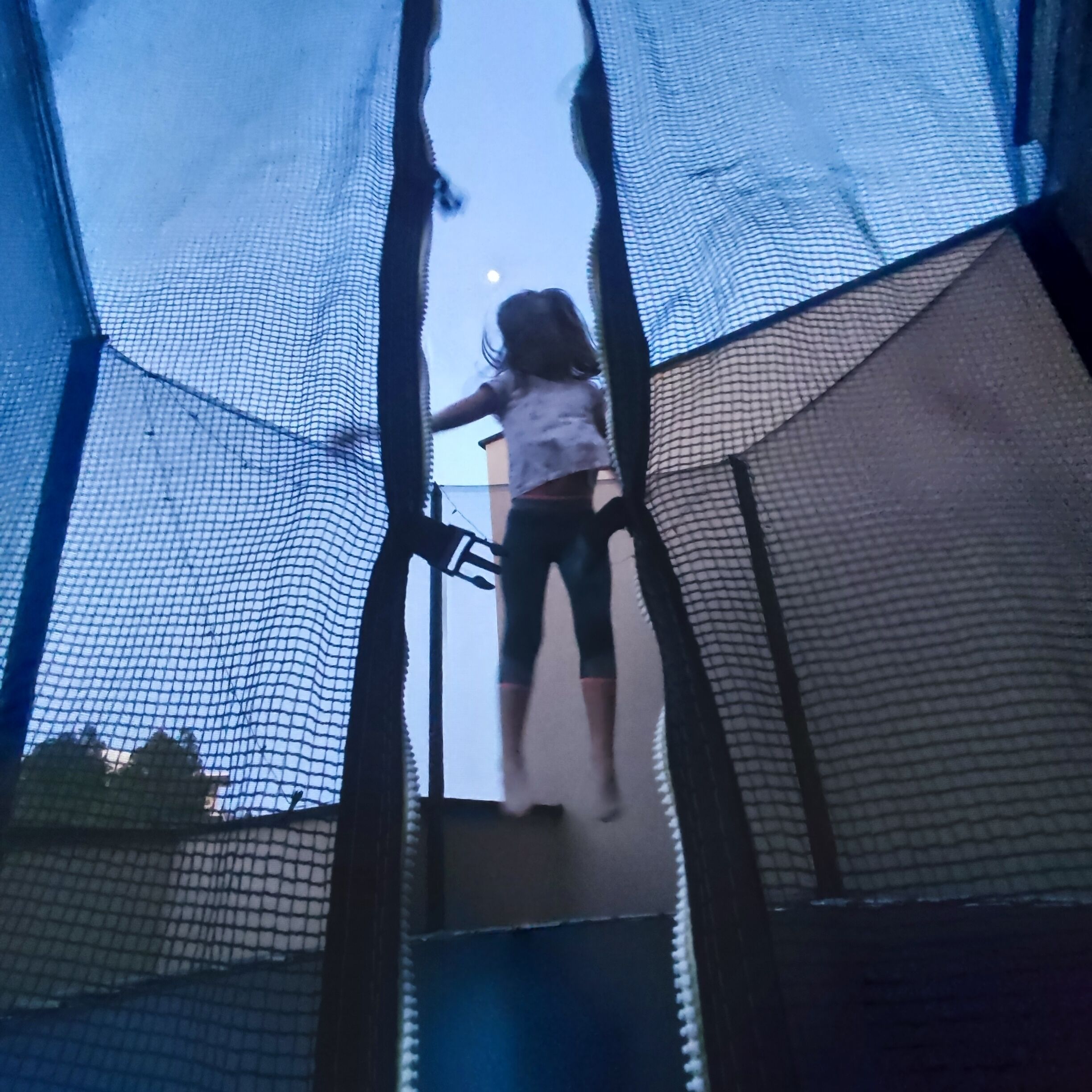 Ein Kind klettert auf einen Trampolin mit Netz an allen Seiten.