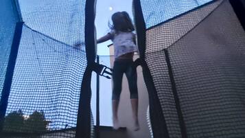 Ein Kind klettert auf einen Trampolin mit Netz an allen Seiten.