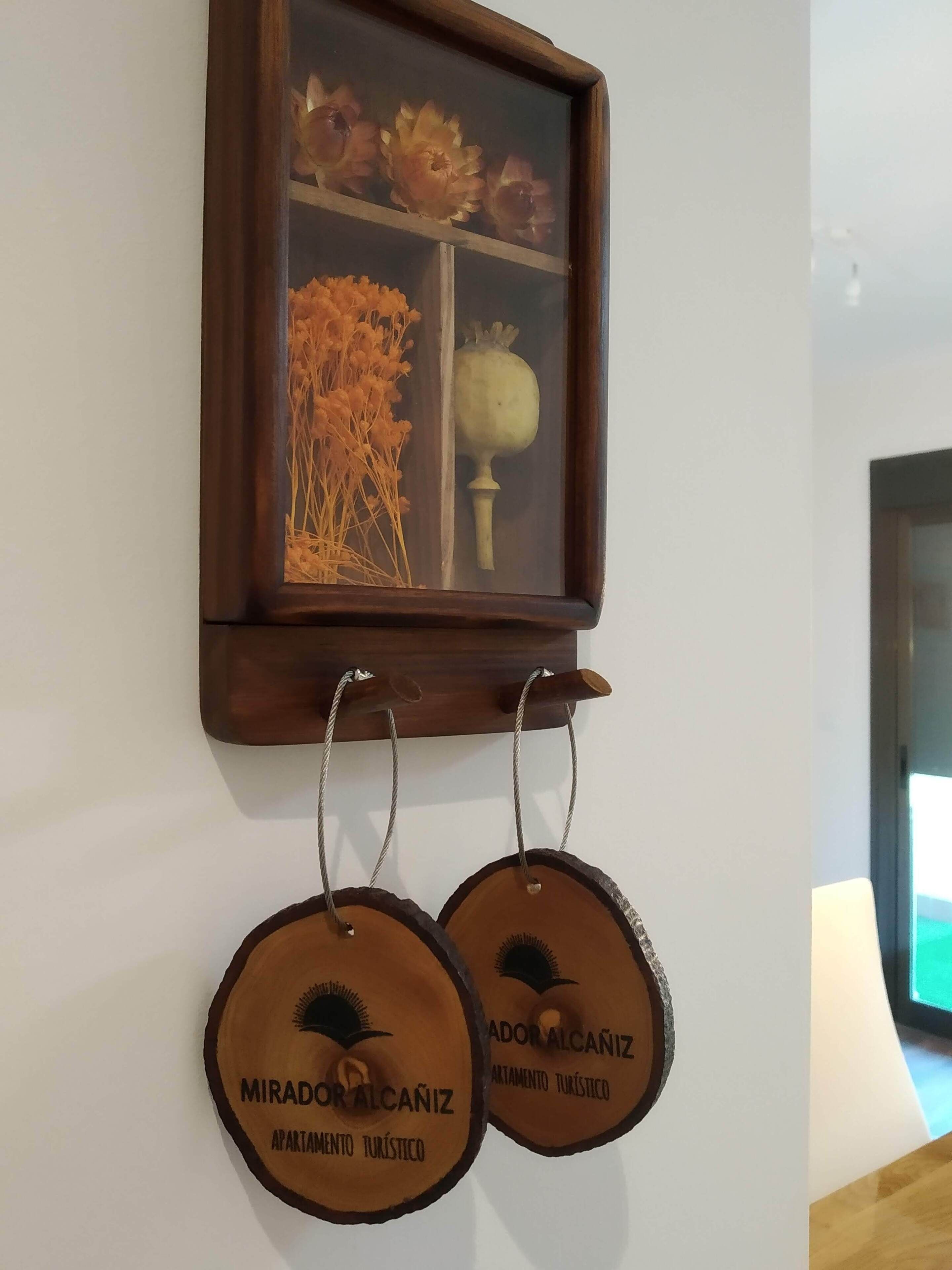 A framed artwork with dried flowers and a poppy on the wall. Below, two wooden plaques with text hang from a wooden rack.