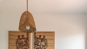 Un coin repas avec une table en bois, des chaises rouges, un luminaire suspendu en fibres tressées et deux œuvres d’art encadrées accrochées au mur.