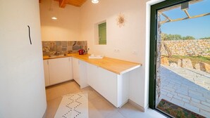 Une cuisine avec des armoires blanches, un plan de travail en bois et une vue sur un mur de pierre à l’extérieur.