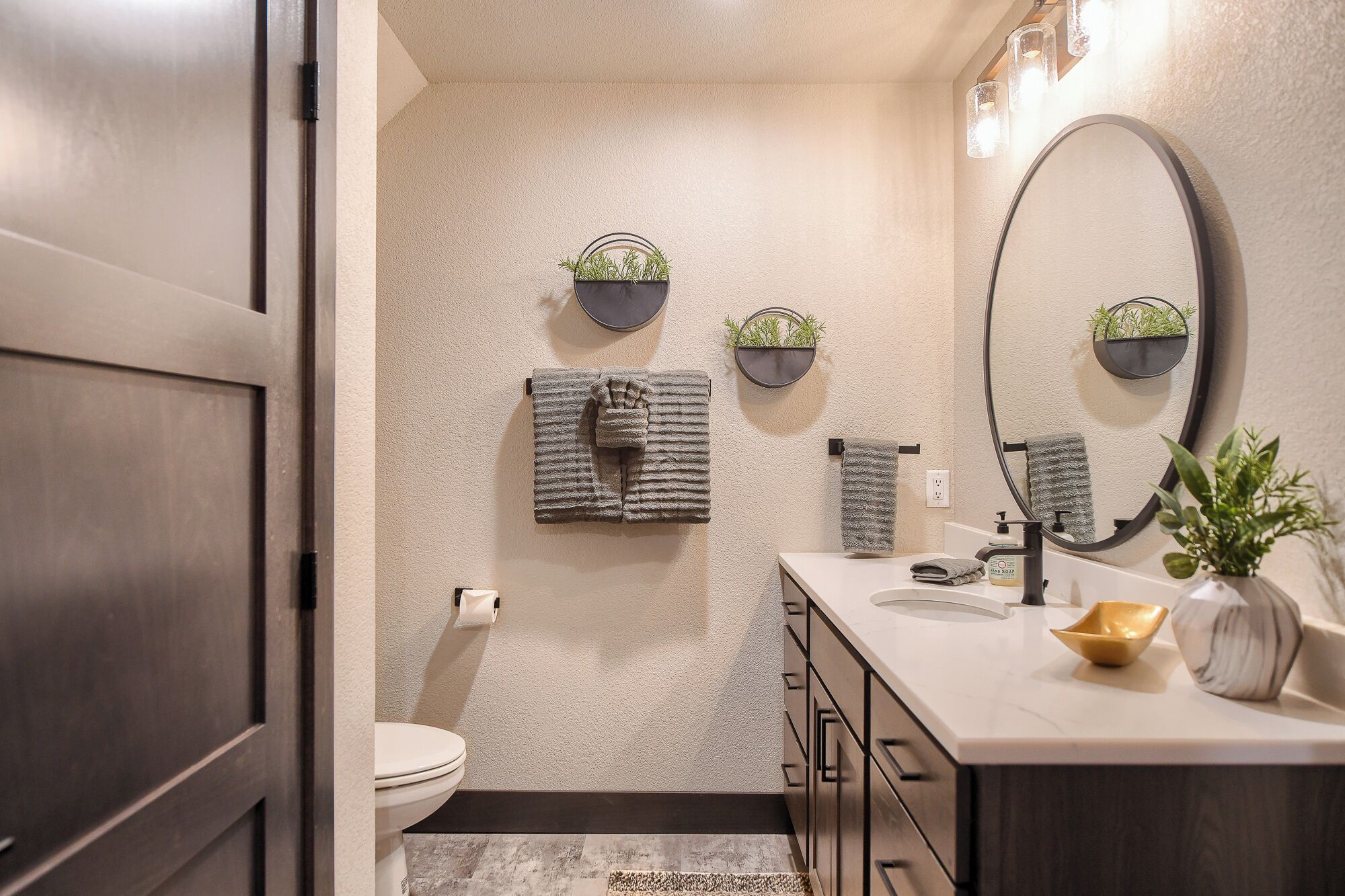 A bathroom with a toilet, a sink, a mirror, and three wall-mounted towel racks with plants.