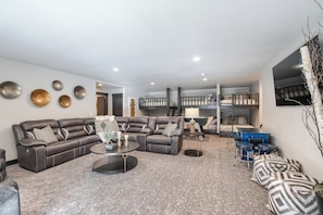 A modern living room with a sectional sofa, a round coffee table, and a bunk bed in the background.