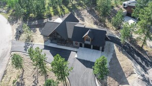 A large, two-story cabin with a steeply pitched roof, surrounded by a forested area. - Open Floor Plan, Walking Distance to Clubhouse, 4400+ Sq. Ft. Large Driveway! (Lead)