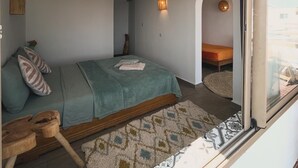 A bedroom with a bed, a wooden bench, a rug, and a small table. - Surf house Maroc (Essaouira)