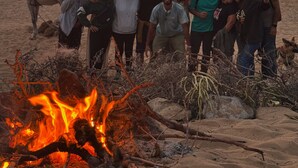A group of people gathered around a campfire on a beach at sunset. - Surf house Maroc (Essaouira)