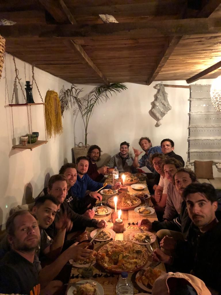 A group of people seated around a table with food, in a room with wooden beams on the ceiling.