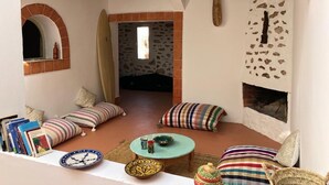 A cozy living room with a fireplace, striped cushions, a small table with a bowl, and a surfboard leaning against the wall. - Surf house Maroc (Essaouira)