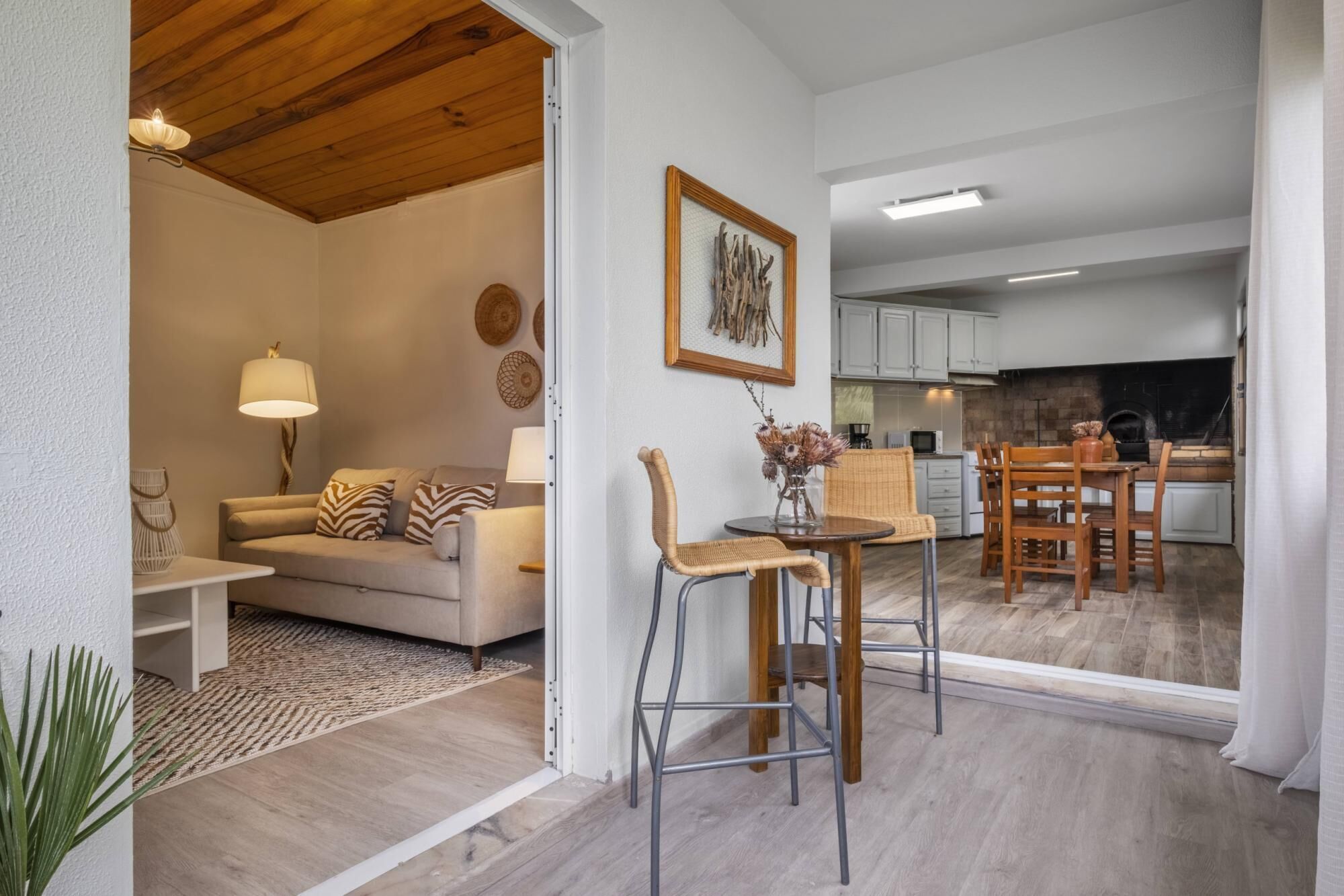 Una sala moderna con un sofá, dos sillones, una mesa de centro y una zona de comedor con mesa y sillas. Se ve una cocina al fondo.