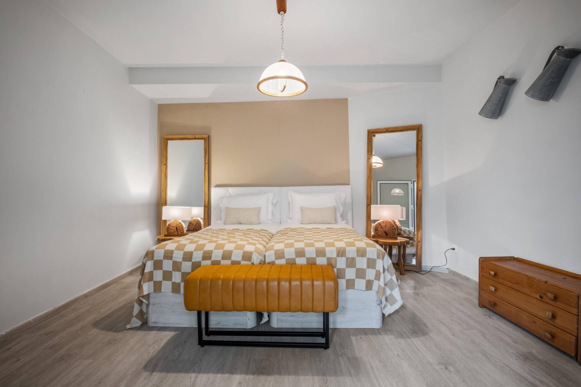 A bedroom with a large bed, a bench, a dresser, and two mirrors.