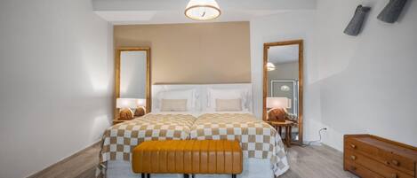 A bedroom with a large bed, a bench, a dresser, and two mirrors.