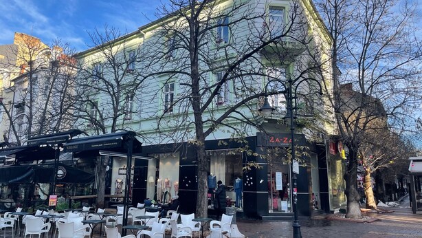 An outdoor cafe with white plastic chairs and tables, a building with a sign reading "ZA-ZA", and bare trees in the background. - The Green Bar House (Sofia)