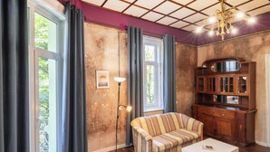 A room with a wooden floor, a striped sofa, a white coffee table, a floor lamp, and a wooden cabinet with glass doors. - The Green Bar House (Sofia)