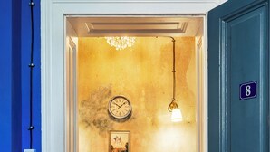 A hallway with a wooden floor, a table with brochures, a clock, a chandelier, and a door with the number 8. - The Green Bar House (Sofia)