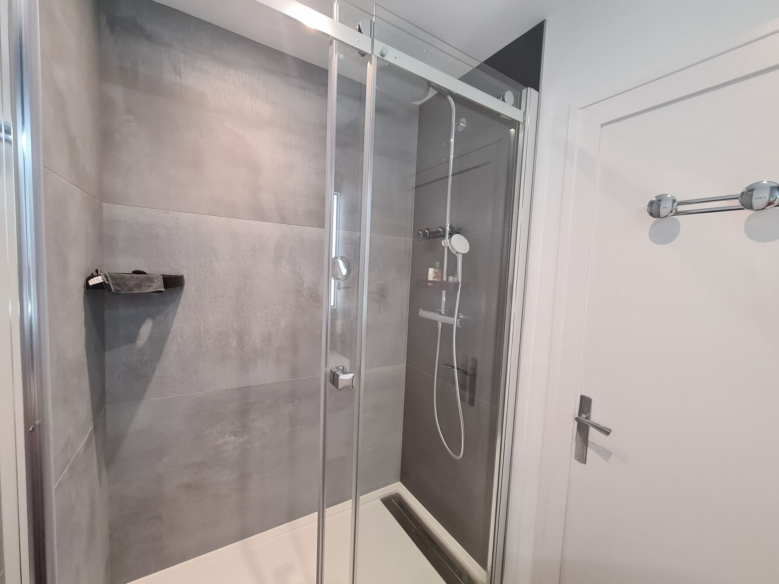 Un baño moderno con ducha de vidrio, toallero y puerta con dispensador de toallas.