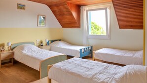 A room with three single beds, wooden flooring, a sloped ceiling, and a window with curtains. - Large family home with garden- For 10 (Penmarch)