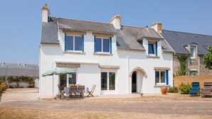 A two-story house with a patio, a table with chairs, and a large potted plant. - Large family home with garden- For 10 (Penmarch)