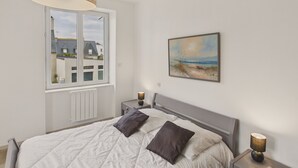 Ein Schlafzimmer mit einem Bett, zwei Nachttischen, einem Fenster und einem Bild an der Wand.