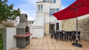 Eine Terrasse mit Steingrill, Sitzgelegenheiten im Freien und einem roten Sonnenschirm.