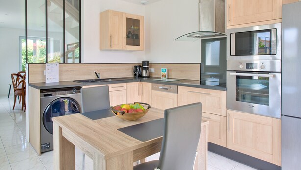 Eine moderne Küche mit Holzausstattung, einem eingebauten Geschirrspüler, einem Edelstahlbackofen und einem Essbereich mit Tisch und Stühlen.