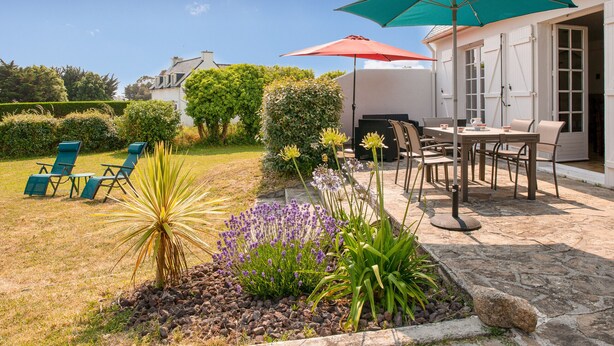 Un patio con mobiliario exterior, suelo de piedra y un jardín con diversas plantas.