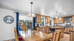 Een moderne keuken met houten kastjes, een eethoek met een houten tafel en stoelen, en een grote klok aan de muur.