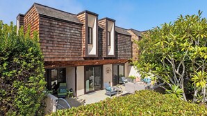 Une maison moderne avec un toit en pente, de grandes fenêtres et un patio aménagé avec du mobilier d’extérieur.