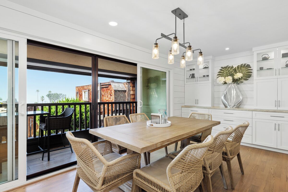 A dining area with a wooden table and wicker chairs, a balcony with a view of a brick building, and white cabinetry with decorative items.