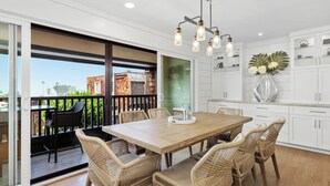Une cuisine moderne avec des meubles blancs, une table à manger en bois, des chaises en osier et un luminaire suspendu.