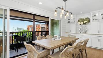 A dining area with a wooden table and wicker chairs, a balcony with a view of a brick building, and white cabinetry with decorative items.