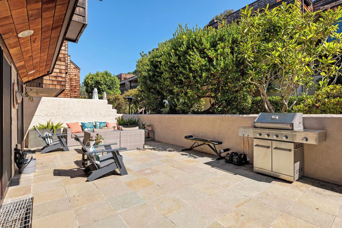 An outdoor patio with a grill, seating area, and a stone floor.