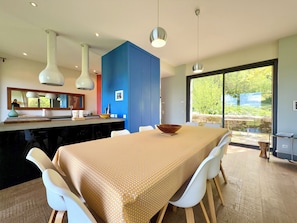 A modern kitchen with a dining area, large windows, and a view of greenery.